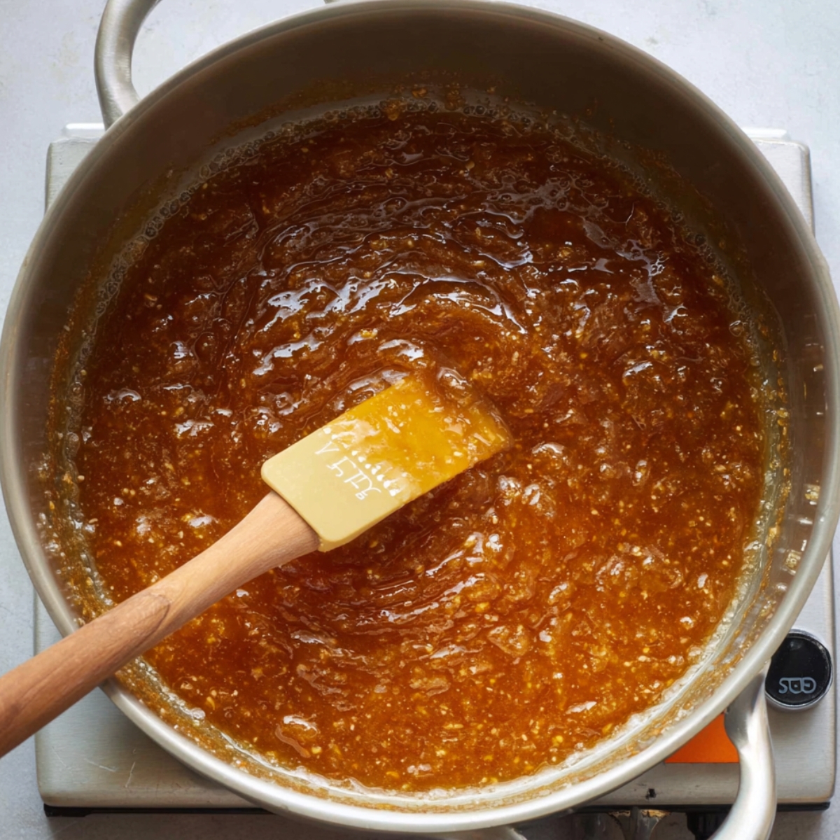 Easy Chocolate Snickers Cake Recipe 10 A rich, golden caramel syrup simmering in a pan, with a wooden spatula stirring the bubbling mixture, ready for use in desserts.