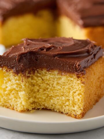 A slice of moist Yellow Cake topped with creamy chocolate frosting, sitting on a plate.