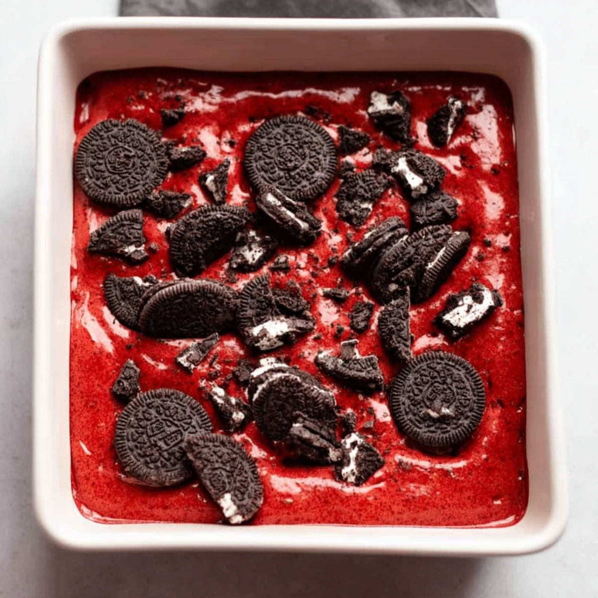 Easy Red Velvet Oreo Brownies Recipe 11 Close-up of a pan filled with red velvet brownie batter topped with crushed Oreos before baking.