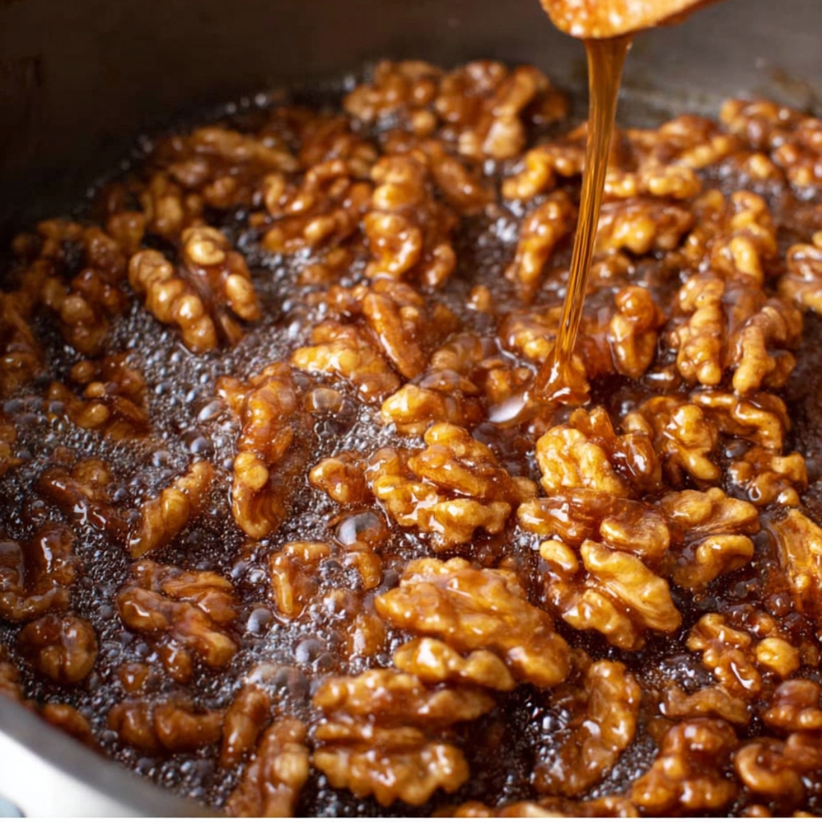 Best Candied Walnuts Recipe 11 Caramel syrup being poured over walnuts, coating them in a glossy glaze.