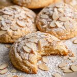 Almond Cookies topped with slivers of almonds and powdered sugar, with one broken to show the interior.