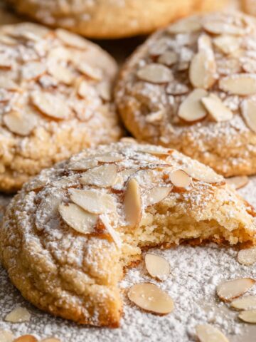 The Best Almond Cookies Recipe 3 Almond Cookies topped with slivers of almonds and powdered sugar, with one broken to show the interior.