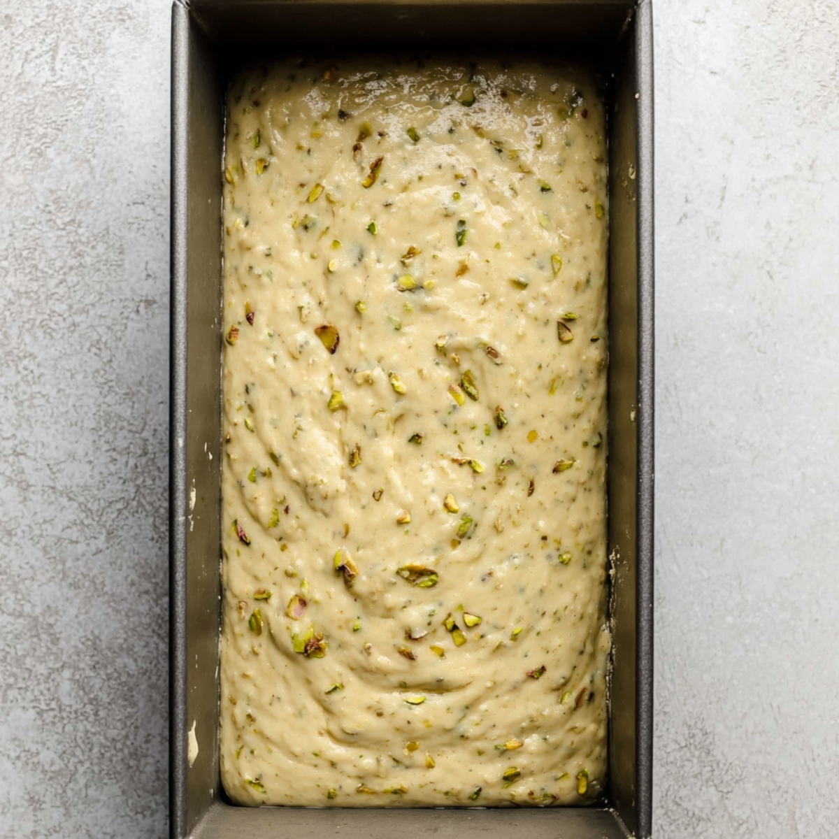 Easy Lemon Pistachio Loaf Recipe 11 Pistachio batter in a loaf pan, ready to be baked. The mixture is smooth with visible pieces of pistachio throughout, giving it texture and flavor.