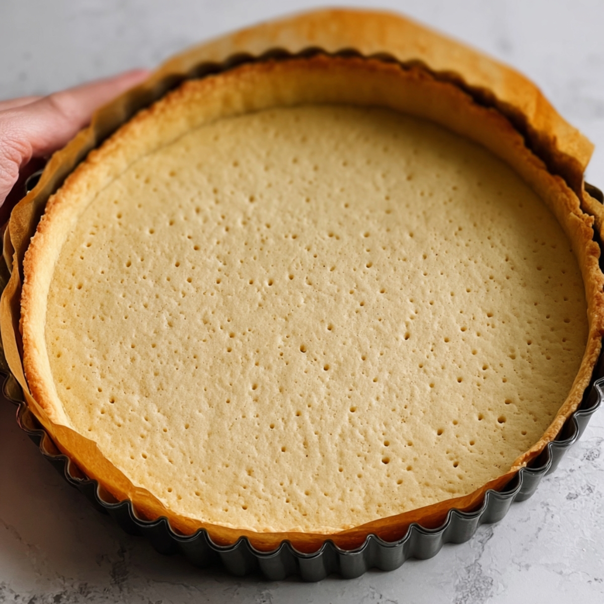 French Raspberry Tart Recipe 11 A golden, baked tart shell with a slightly crimped edge, resting in a tart pan. The crust is smooth and even with tiny holes pricked into it.