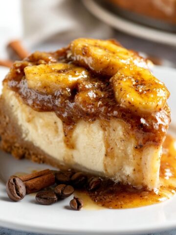 Easy Bananas Foster Cheesecake Recipe 1 A slice of Bananas Foster Cheesecake with caramelized banana topping and syrup on a white plate.