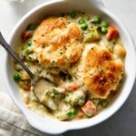 Biscuit Vegetable Pot Pie Casserole with golden, flaky biscuit topping, featuring a creamy mixture of peas, carrots, and broccoli in a white casserole dish.