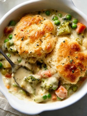 Biscuit Vegetable Pot Pie Casserole 3 Biscuit Vegetable Pot Pie Casserole with golden, flaky biscuit topping, featuring a creamy mixture of peas, carrots, and broccoli in a white casserole dish.