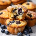 Freshly baked blueberry muffins with a golden top, one muffin split open to reveal juicy blueberries inside.