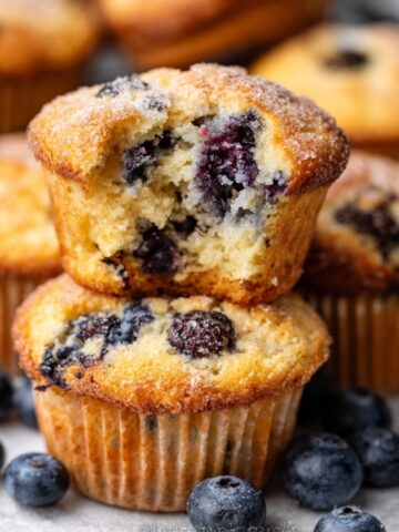 Freshly baked blueberry muffins with a golden top, one muffin split open to reveal juicy blueberries inside.
