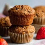 Freshly baked bran muffins, golden and crisp on top, stacked and ready to be enjoyed, with a side of strawberries.
