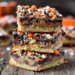 Stack of three Candy Cookie Bars, filled with chocolate and caramel, topped with orange, black, and white sprinkles.