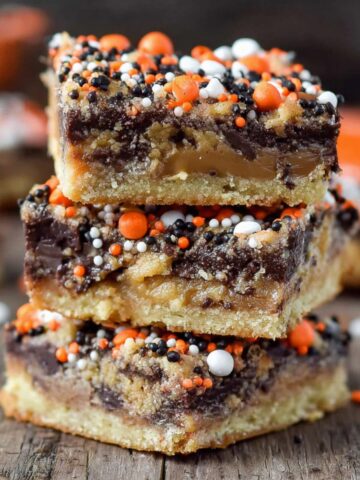 Stack of three Candy Cookie Bars, filled with chocolate and caramel, topped with orange, black, and white sprinkles.