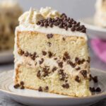 A slice of cannoli cake with chocolate chip filling, topped with mini chocolate chips, showcasing soft cake layers and creamy frosting.