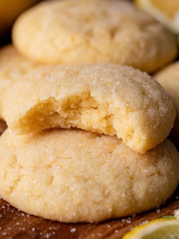 Chewy Lemon Sugar Cookies 2 Golden Chewy Lemon Sugar Cookies, one broken open, with lemon slices and flowers.