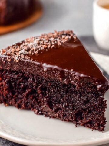 Best Chocolate Gooey Butter Cake Recipe 2 A slice of Chocolate Gooey Butter Cake with a rich, glossy ganache topping, served on a white plate, showcasing the moist interior.