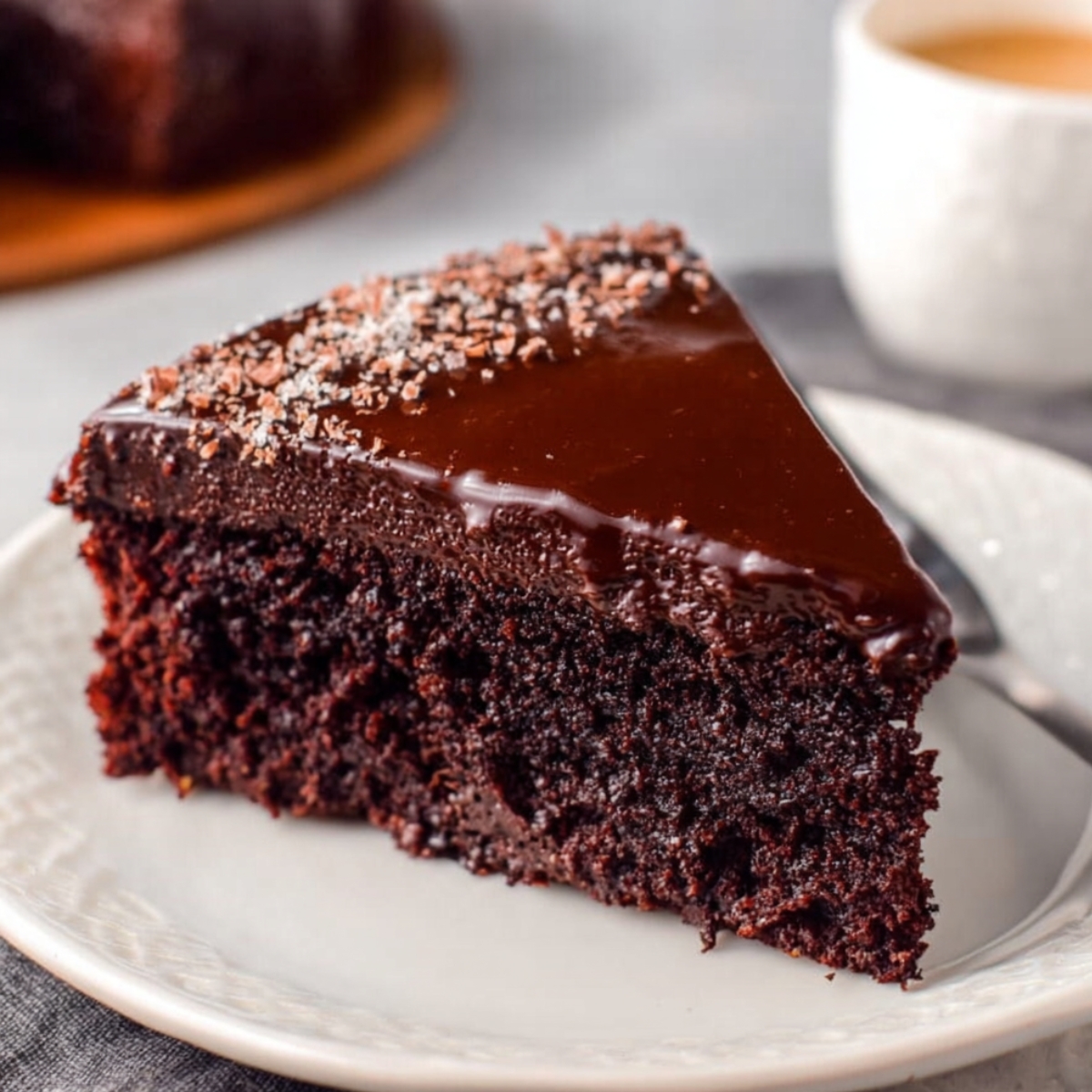 A slice of Chocolate Gooey Butter Cake with a rich, glossy ganache topping, served on a white plate, showcasing the moist interior.