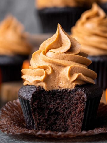 Easy Chocolate Pumpkin Cupcakes Recipe 3 Chocolate Pumpkin Cupcakes with pumpkin frosting and a bite taken out.