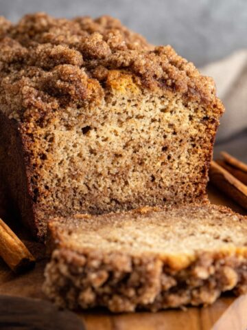 Easy Cinnamon Streusel Banana Bread 1 A freshly baked loaf of Cinnamon Streusel Banana Bread with a crumbly cinnamon streusel topping, sliced to reveal its soft, moist interior. The loaf is accompanied by cinnamon sticks and a cozy kitchen backdrop.