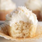 Fluffy Coconut Cupcakes with a bite taken out, topped with coconut flakes and creamy frosting.
