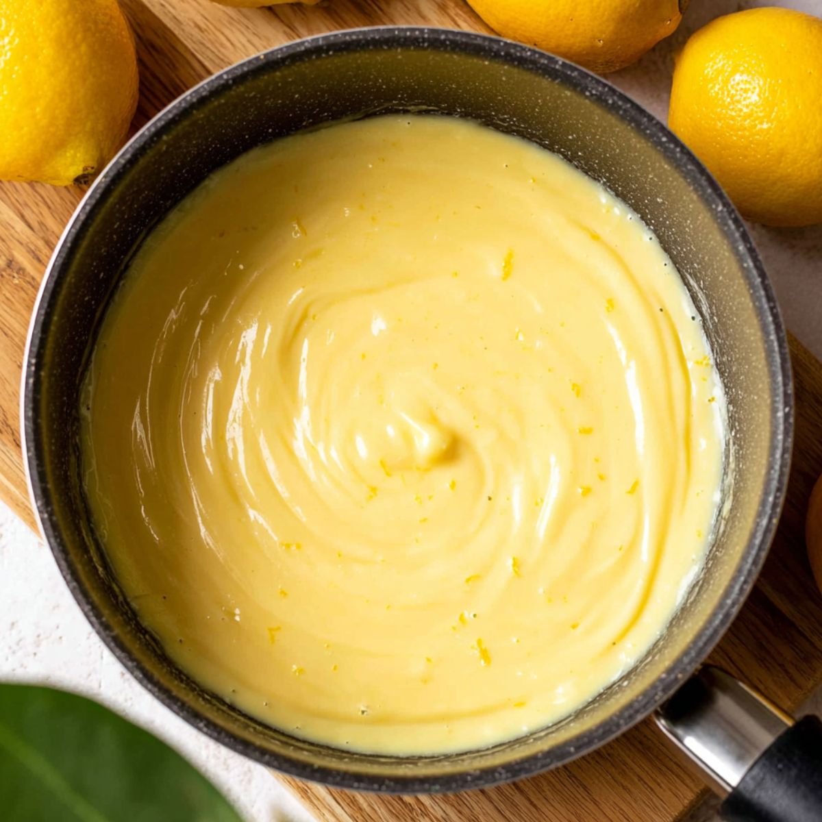 Lemon Crème Brûlée Cookies 10 A smooth lemon custard filling, swirling gently in a saucepan with visible lemon zest mixed into the creamy yellow texture, surrounded by fresh lemons.