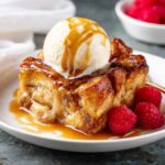 Croissant Bread Pudding slice with a scoop of vanilla ice cream on top and raspberry garnish.