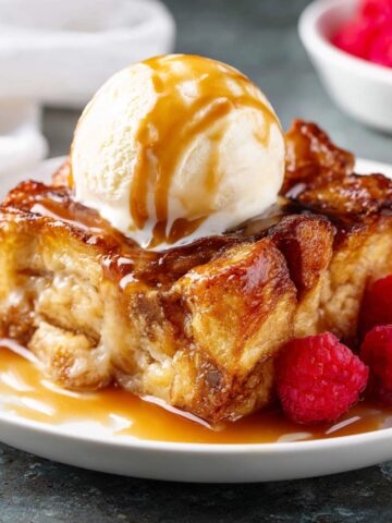 Easy Croissant Bread Pudding Recipe 1 Croissant Bread Pudding slice with a scoop of vanilla ice cream on top and raspberry garnish.