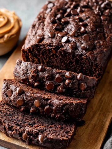 Double Chocolate Banana Bread 4 Freshly baked loaf of Double Chocolate Banana Bread, sliced into pieces and topped with chocolate chips. A bowl of peanut butter sits in the background.