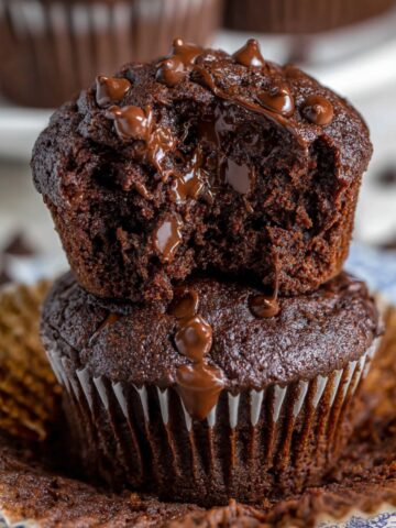 Moist Double Chocolate Muffins Recipe 1 A freshly baked Double Chocolate Muffins with a gooey, melted chocolate center and a sprinkle of chocolate chips on top, served on a plate with the muffin wrapper peeled away.