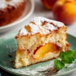 A slice of Fresh Peach Cake dusted with powdered sugar, placed on a green plate.