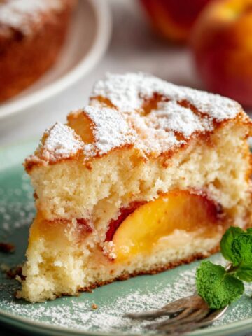 Fresh Peach Cake Recipe 2 A slice of Fresh Peach Cake dusted with powdered sugar, placed on a green plate.