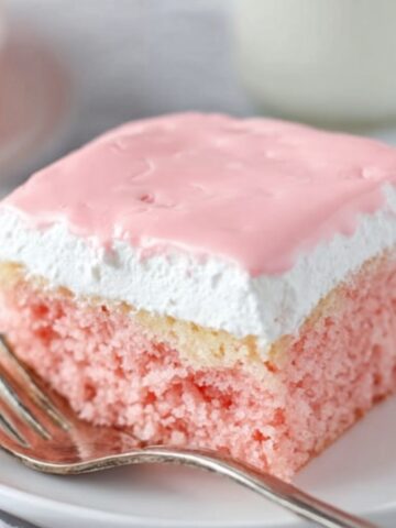 Easy Hawaiian Guava Cake Recipe 1 A slice of pink Hawaiian Guava Cake topped with white whipped cream and a smooth, pastel pink glaze, served on a white plate with a silver fork beside it.