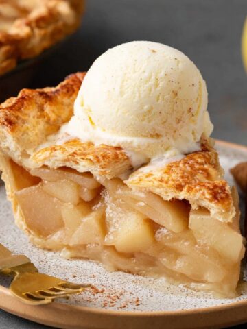 Homemade Pear Pie Recipe 3 A slice of Homemade Pear Pie with a golden flaky crust, topped with a scoop of vanilla ice cream. The tender pear filling is visible inside, and cinnamon sticks sit beside the plate for added flavor.