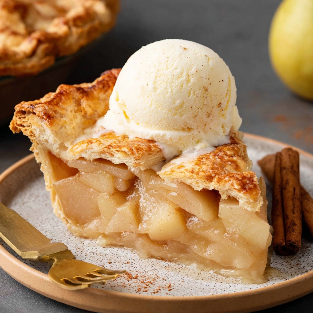 A slice of Homemade Pear Pie with a golden flaky crust, topped with a scoop of vanilla ice cream. The tender pear filling is visible inside, and cinnamon sticks sit beside the plate for added flavor.