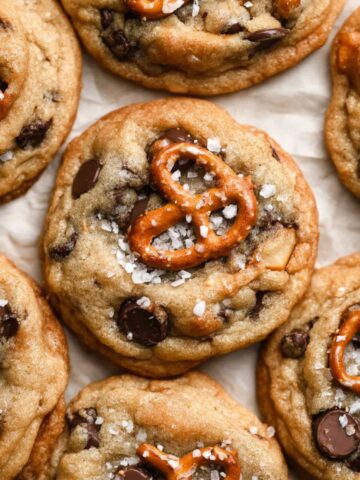 Close-up of freshly baked Kitchen Sink Cookies with pretzels, chocolate chips, and a sprinkle of sea salt on top, arranged on parchment paper.