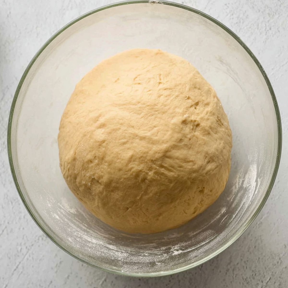 Best Maple Pecan Sticky Buns Recipe 10 A ball of dough resting in a glass bowl, lightly dusted with flour, ready for the next step in baking.
