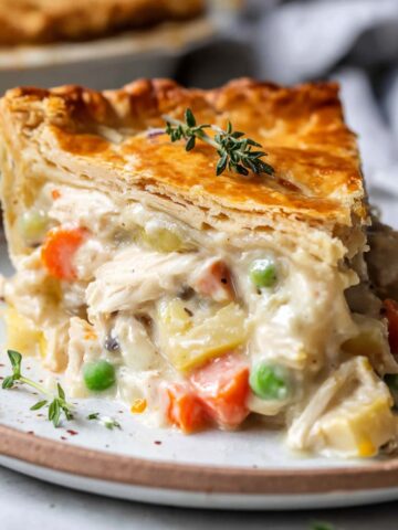 A slice of Leftover Turkey Pot Pie on a plate, showing a creamy filling of vegetables and chicken, with a golden, flaky crust and garnished with a sprig of thyme.