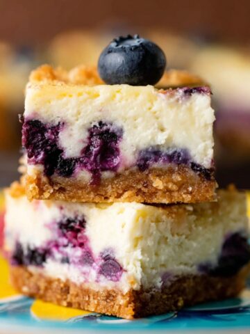 Stacked Lemon Blueberry Cheesecake Bars with a graham cracker crust and topped with a fresh blueberry.