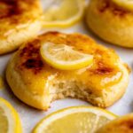 A freshly baked Lemon Crème Brûlée Cookies with a golden caramelized top, garnished with a fresh slice of lemon, showing a bite taken out revealing the soft interior.