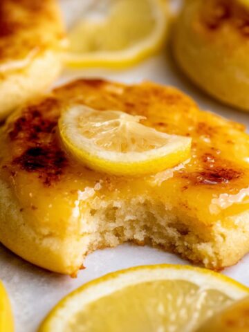 Lemon Crème Brûlée Cookies 1 A freshly baked Lemon Crème Brûlée Cookies with a golden caramelized top, garnished with a fresh slice of lemon, showing a bite taken out revealing the soft interior.