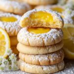 A stack of Lemon Curd Cookies, dusted with powdered sugar, with one cookie broken in half to reveal the smooth lemon curd filling inside.