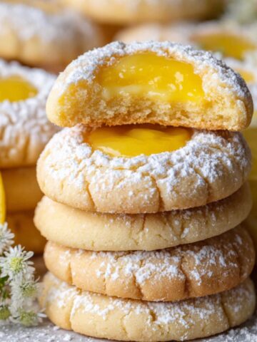 The Best Lemon Curd Cookies Recipe 2 A stack of Lemon Curd Cookies, dusted with powdered sugar, with one cookie broken in half to reveal the smooth lemon curd filling inside.