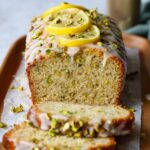 Freshly baked Lemon Pistachio Loaf with a sweet glaze on top, garnished with lemon slices and chopped pistachios, showcasing the soft, moist interior with visible pistachio bits.