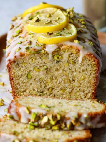 Easy Lemon Pistachio Loaf Recipe 4 Freshly baked Lemon Pistachio Loaf with a sweet glaze on top, garnished with lemon slices and chopped pistachios, showcasing the soft, moist interior with visible pistachio bits.