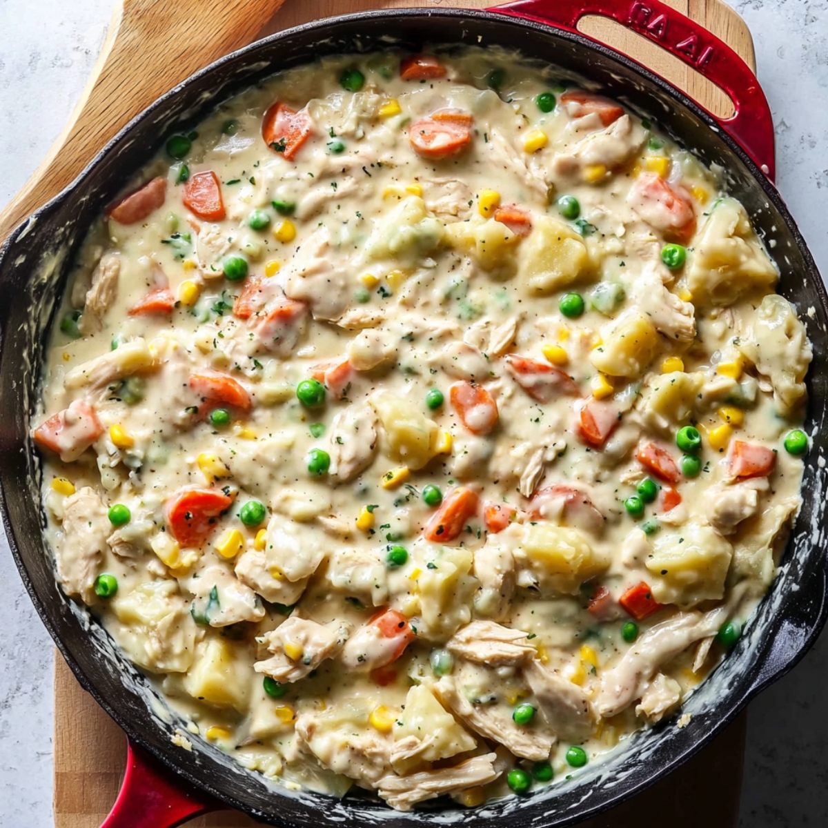 Homemade Leftover Turkey Pot Pie Recipe 10 A skillet filled with a creamy chicken and vegetable mixture, including carrots, peas, and potatoes, simmering in a savory sauce.