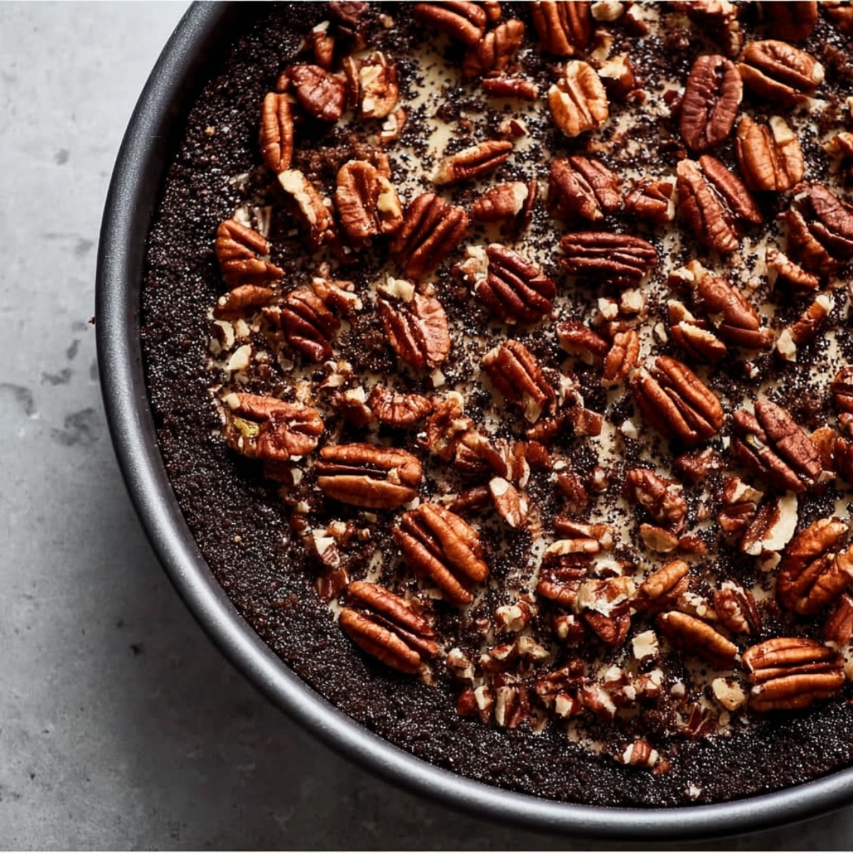 Best Caramel Turtle Cheesecake Recipe 10 The dark crust of a cheesecake, topped with toasted pecans scattered evenly across the surface, creating a delicious and crunchy base.