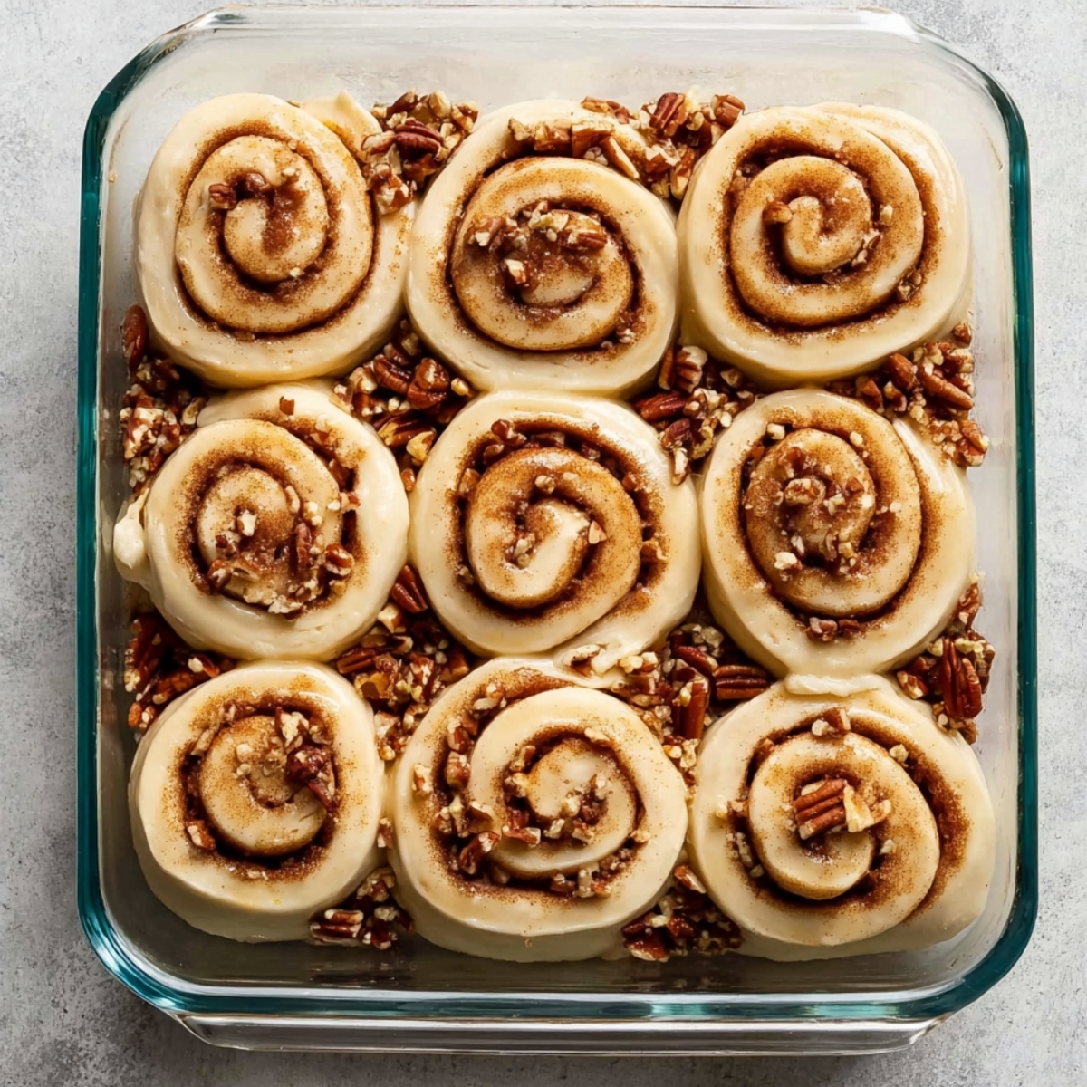 Best Maple Pecan Sticky Buns Recipe 11 A baking dish filled with unbaked cinnamon rolls, topped with cinnamon-sugar swirl and chopped pecans, ready to be baked.