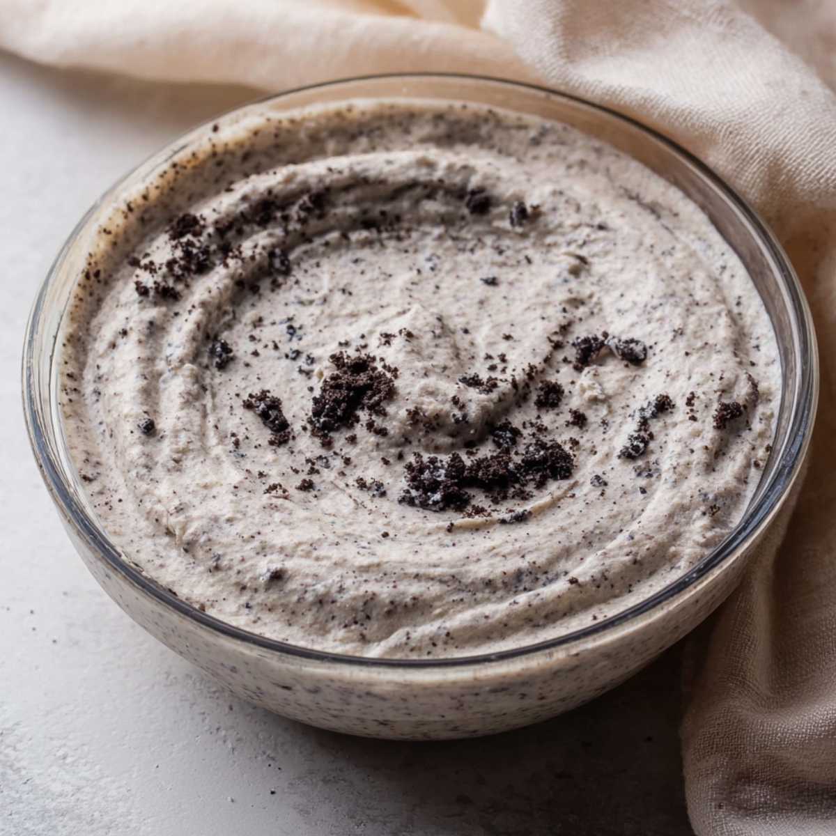 The Best Oreo Pie Recipe 11 A glass bowl filled with creamy Oreo cookie filling, topped with small bits of Oreo crumbs, giving a textured appearance."