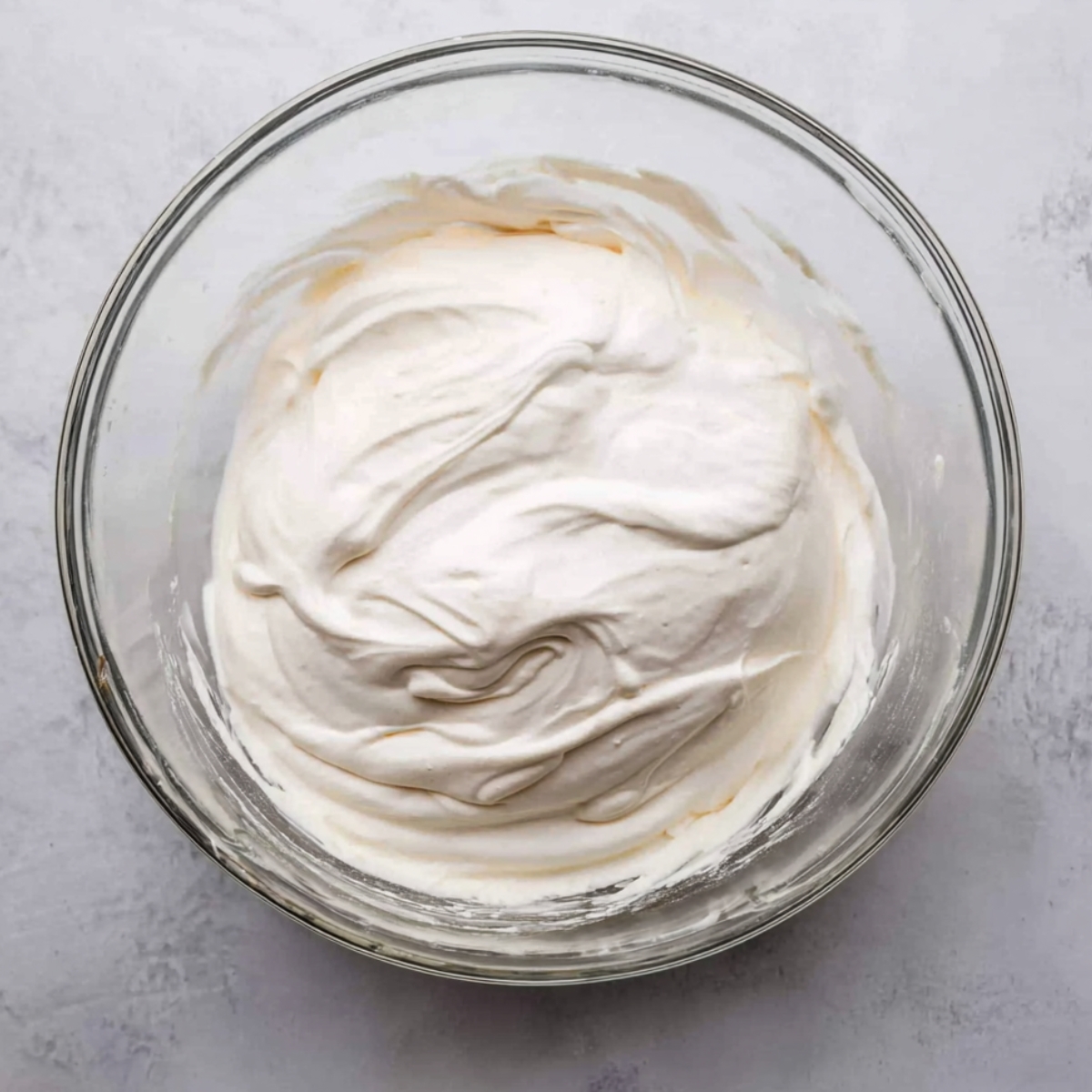 The Best Cannoli Cake Recipe 11 Whipped cream or frosting mixture in a glass bowl, showing a soft and airy texture.