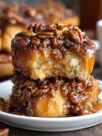 Best Maple Pecan Sticky Buns Recipe 3 A close-up of Maple Pecan Sticky Buns, glistening with caramel syrup and crunchy pecans, stacked on a plate.