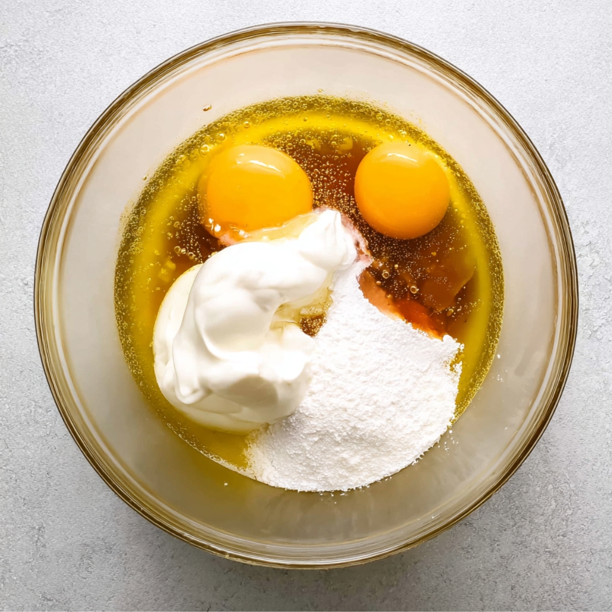 Chocolate Olive Oil Cake Recipe 10 Wet ingredients for a cake, including eggs, vanilla, sugar, sour cream, and oil, mixed in a glass bowl.